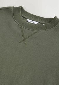 Oliivinvihreä, pyöreäkauluksellinen collegepaita, jossa on resorikaulus ja edessä ommeltu V-yksityiskohta, NEXT-merkintä kauluksen sisäpuolella.