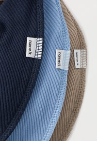 Τρία ριμπ βαμβακερά καπέλα σε ναυτικό μπλε, ανοιχτό γαλάζιο και καφέ, το καθένα με μια μικρή ετικέτα «name it». Τα καπέλα είναι τακτοποιημένα στοιβαγμένα.