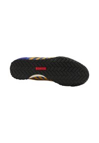 La chaussure de sport K-Swiss présente une semelle extérieure en caoutchouc noir durable avec un motif en chevrons, et un dessus multicolore avec des rayures bleues et jaunes.