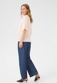 Bluză roz deschis, cu mânecă scurtă, cu un croi lejer, asociată cu blugi din denim de culoare albastru închis, cu talie înaltă și picioare ample, și mule negre cu toc.