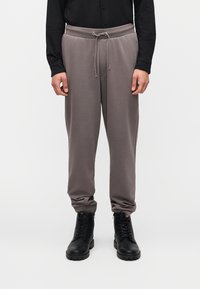 Γκρι φόρμα με ελαστική μέση και ρυθμιζόμενο κορδόνι. Διαθέτει πλαϊνές τσέπες και στενά μανσέτες, συνδυασμένα με μαύρα μποτάκια με κορδόνια.