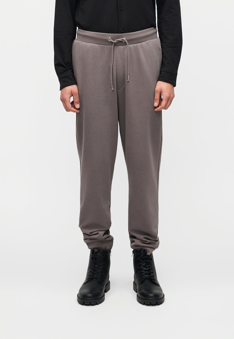 Γκρι φόρμα με ελαστική μέση και ρυθμιζόμενο κορδόνι. Διαθέτει πλαϊνές τσέπες και στενά μανσέτες, συνδυασμένα με μαύρα μποτάκια με κορδόνια.