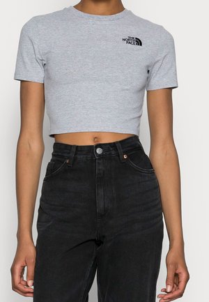 Person trägt ein hellgraues, kurz geschnittenes T-Shirt mit "The North Face"-Logo und hoch taillierte schwarze Jeans, steht mit entspannten Armen.