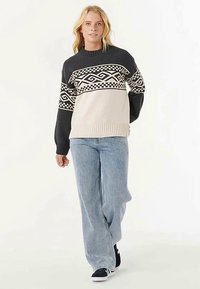 Strikket sweater med en blanding af sort, creme og grå. Indeholder geometriske mønstre på tværs af brystet og ribbet kant. Kombination med lyse jeans.