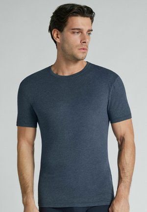 Mand med kort mørkt hår iført en tætsiddende mørkeblå rundhalset T-shirt, der kigger mod højre mod en ensartet lys baggrund.