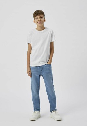Vit bomulls-t-shirt, blå denimjeans med avslappnad passform, kombinerade med vita sneakers. Enkel design, utan mönster eller utsmyckningar.