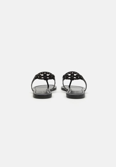 Sandales plates noires avec un design de lanière tissée, semelle en caoutchouc lisse et forme minimaliste. Aucun embellissement supplémentaire n'est présent.