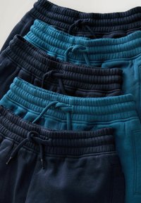 Fünf Paar Jogginghosen in verschiedenen Schattierungen von Marineblau und Teal, mit elastischen Taillenbündchen und Kordelzügen, auf einem flachen Untergrund gestapelt.