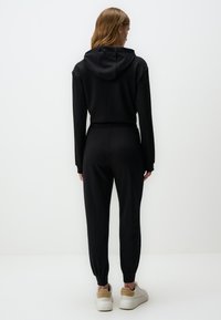 Zwarte hoodie gecombineerd met slim-fit joggers. De hoodie heeft een relaxte pasvorm; de joggers hebben een elastische tailleband en boorden.