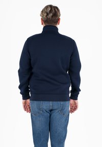 Felpa blu navy con colletto alto, polsini e orlo a coste. Indossata con jeans azzurri, vista concentrata sul retro del capo.
