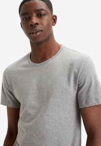 Tricou din bumbac gri cu guler rotund, mâneci scurte și o textură moale, având cusături minime și fără modele sau accente vizibile.