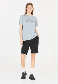 Ljusgrå t-shirt med kort ärm och grafik av berg och träd; svarta shorts med dragkedjefickor; svarta sneakers och vita strumpor.