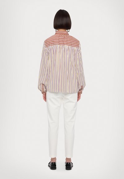 Striped long-sleeve shirt featuring vertical lines in red, yellow, and purple; button cuffs and a classic collar. Paired with white trousers.