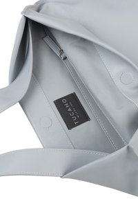 Interno di una borsa tote in finta pelle grigia con dettagli cuciti, una tasca con zip e un'etichetta in tessuto nera con la scritta "Tucano Milano 1985."