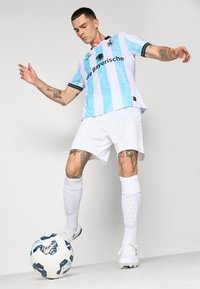Šviesiai mėlynos ir baltos juostelės futbolo marškiniai su juodais akcentais, balti šortai, iki kelių siekiančios baltos kojinės ir raštuotas futbolo kamuolys ant žemės.