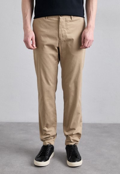 Chinos caqui hechos de una tela suave, con un diseño de pierna recta y un cierre de botón, combinados con zapatillas negras.
