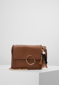 Borsa a tracolla in pelle marrone con chiusura a patta, accentata da un anello dorato e nappine decorative in nero, bianco e marrone. Inclusa tracolla a catena.