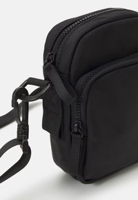 Borsa a tracolla nera in nylon con doppia chiusura a zip, tracolla regolabile e moschettone. Presenta una texture liscia e una forma rettangolare.