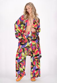 Färgglad, överdimensionerad kimono-stil topp med livligt abstrakt mönster, tillsammans med vida byxor i liknande tryck och orange plattformssandaler.