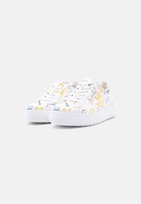 Λευκά παπούτσια χαμηλής κορυφής με πολύχρωμες ζωγραφιές, που περιλαμβάνουν στέμματα, αστέρια, καρδιές και βέλη, εμφανίζονται σε μια απλή λευκή επιφάνεια.