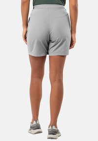 Graue Sportshorts mit glatter Textur, elastischem Bund und Seitentaschen, kombiniert mit grauen und weißen Sneakers.