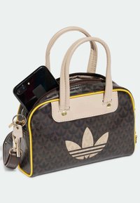 Borsa con motivo nero e marrone, accenti beige, rifiniture gialle, doppio manico e cerniera. Un telefono cellulare è parzialmente visibile all'interno.