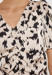 Blusa crema con motivo astratto nero, scollatura a V, maniche corte a palloncino e dettagli arricciati nella parte anteriore. Texture setosa.