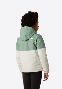 Veste à capuche avec un haut vert menthe et une partie inférieure blanche. Comprend des poignets élastiques et un logo au dos près de l'encolure.