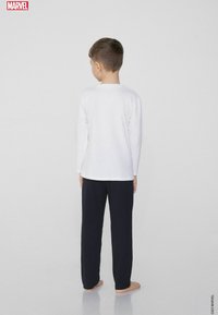 Biała koszula z długimi rękawami i granatowe spodnie na dziecku, widok od tyłu. Prosty fason bez grafik ani wzorów.