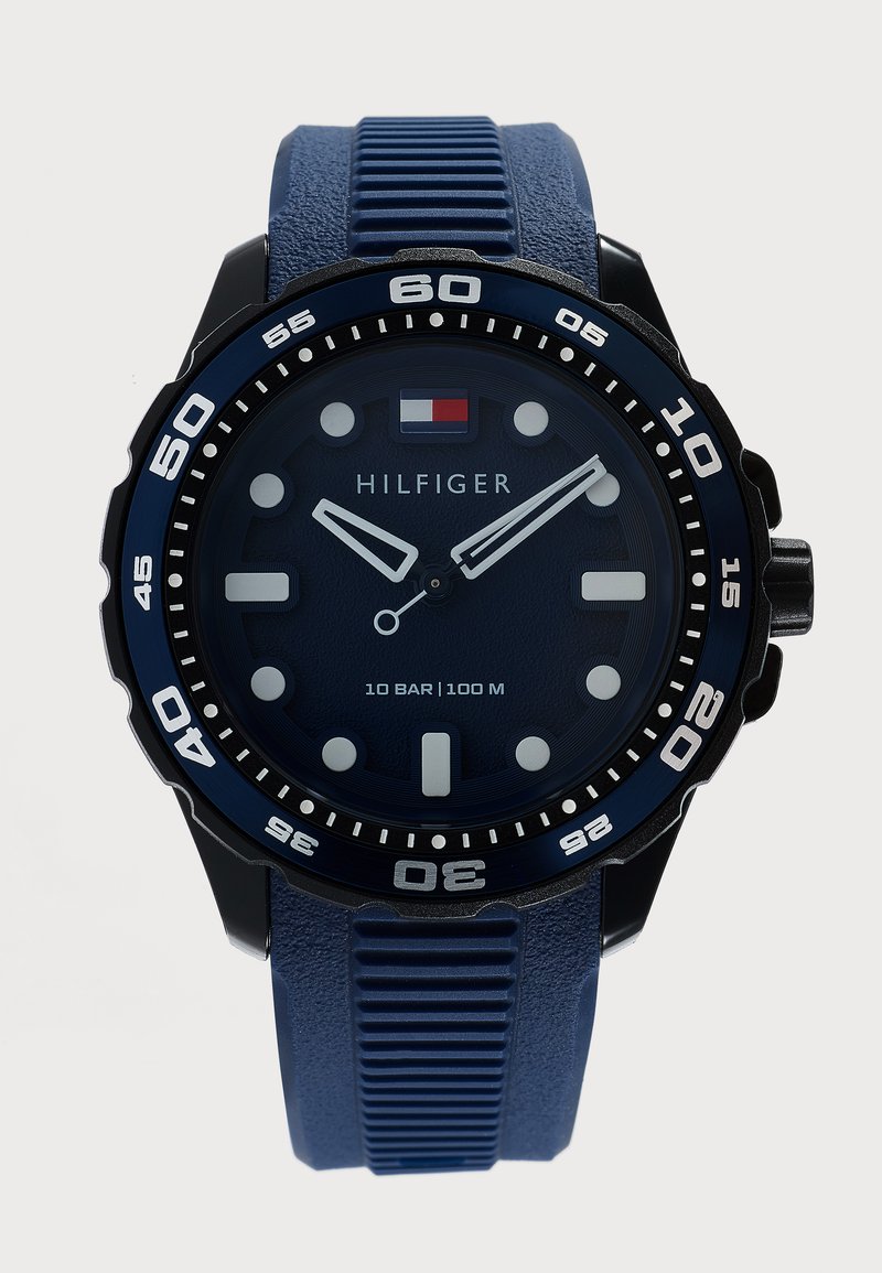 Μπλε αναλογικό ρολόι Tommy Hilfiger με στρογγυλό καντράν, λευκούς δείκτες, περιστρεφόμενο στεφάνι και μπλε υφασμένη σιλικόνη λουράκι.