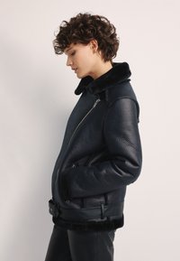 Granatowa skórzana kurtka z sztucznym futrem przy kołnierzu i mankietach, z boku zapinana na zamek i o zdefiniowanej sylwetce. Teksturalna powierzchnia i dopasowany krój.