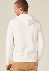 Weißer Hoodie aus strukturiertem Stoff, mit langen Ärmeln und einem kleinen Schlitz im Rücken. Mit einer einstellbaren Kapuze und lässiger Passform.