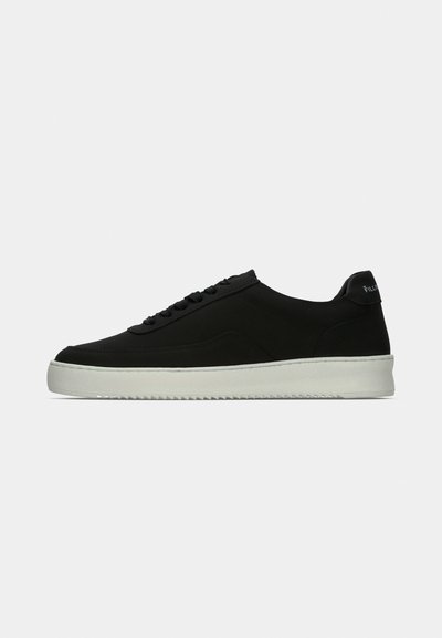 Scarpa da ginnastica nera bassa con lacci neri, suola spessa bianca e linguetta sul tallone su sfondo grigio chiaro uniforme.