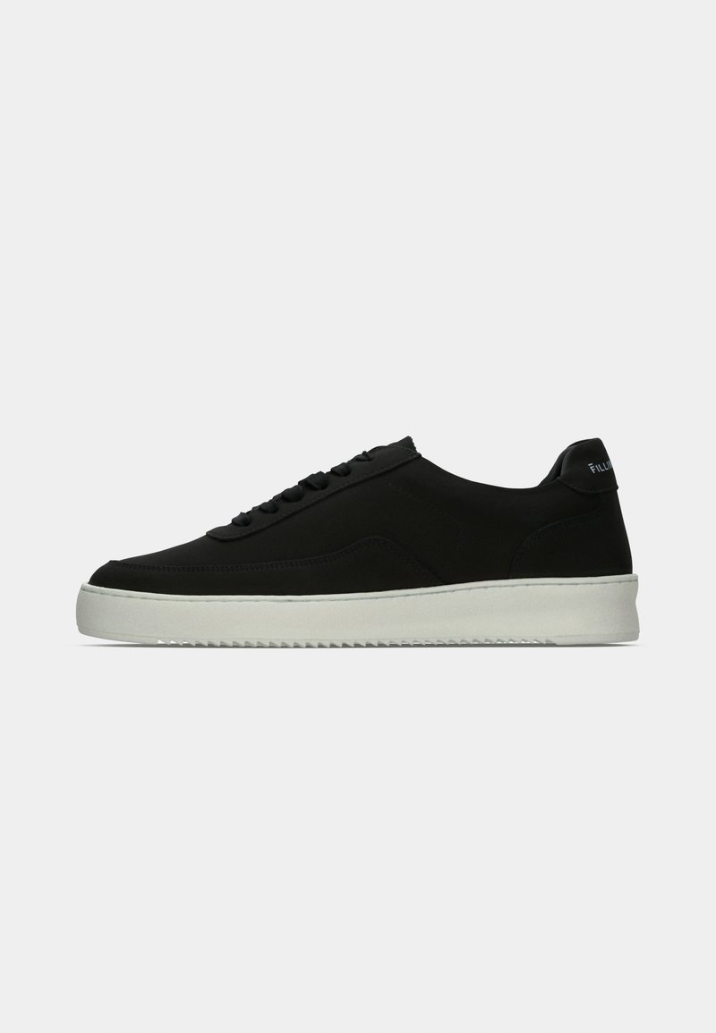 Black low-top sneaker with black laces, white thick sole, and pull tab at heel against a plain light gray background.