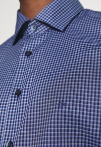 Blå och vit rutad skjorta med knapp-ner krage, prydd med mörka knappar och en liten broderad logotyp på bröstet.