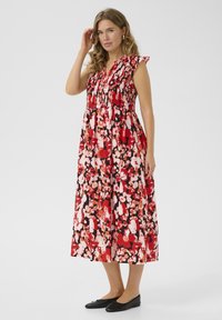 Robe maxi en motif floral rouge, rose et noir ; présente un corsage smocké, des manches volantes, une jupe fluide et un tissu léger.