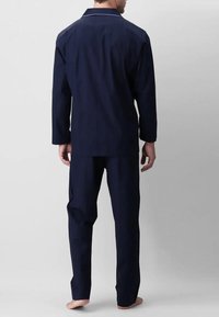 Completo pigiama blu navy composto da una camicia a maniche lunghe con bottoni, rifinita con piping bianco, e pantaloni abbinati, caratterizzati da una vestibilità comoda e senza motivi visibili.