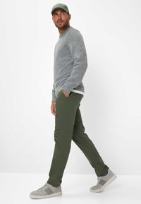 Grijs gebreid sweater, olijfgroene broek en grijze sneakers. De sweater heeft geribbelde manchet; de pet is groen. Eenvoudig ontwerp, casual uitstraling.