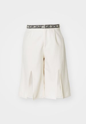 Calções brancos ajustados com uma cintura preta adornada, fendas laterais e um tecido suave e texturizado para maior conforto.