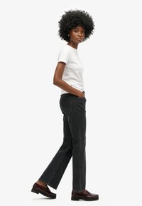 Vaqueros negros de pierna recta con un ajuste de tiro medio y diseño clásico de cinco bolsillos, combinados con una camiseta blanca ajustada y mocasines marrones.