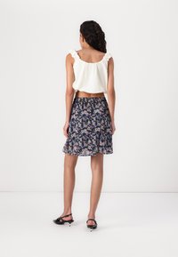 Blouse blanche avec des bretelles volantes, associée à une jupe florale bleu marine à taille élastique et à ourlet fluide. Sandales à brides noires.