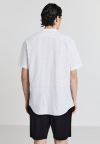 Beige Kurzarmhemd mit Kragen und vertikalen blauen Streifen. Der Stoff wirkt leicht und hat eine glatte Textur, eine taillierte Passform und einen abgerundeten Saum.