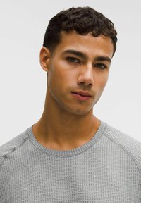 Cămașă texturată gri cu decolteu rotund și mâneci raglan. Țesătura prezintă un model subtil cu puncte mici. Finisaj neted, stil casual.