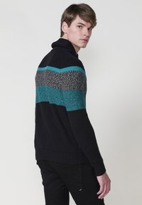 Suéter de hombre en azul marino con punto texturizado; presenta rayas verticales en azul verdoso, gris y negro. El diseño se completa con un cuello doblado y puños acanalados.