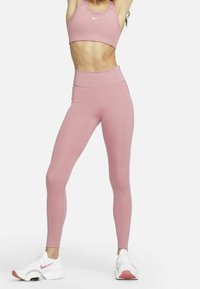 Rosa träningsoutfit bestående av en kort topp och högmidjade leggings, tillverkad av elastiskt material, kombinerad med vita sneakers.