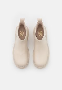Botines de cuero beige hasta el tobillo con punteras redondeadas, paneles laterales elásticos y lengüetas. Presentan una textura suave y un diseño minimalista.