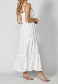 Vit maxiklänning med blommönster i ögonlapp, lagerdesign och justerbara band. Bärs med genomskinliga klacksandaler.