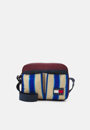 Pieni suorakaiteen muotoinen olkalaukku, jossa on viininpunainen yläosa, beige etutaskut sinisillä raidoilla ja Tommy Jeans -logoplaatta.