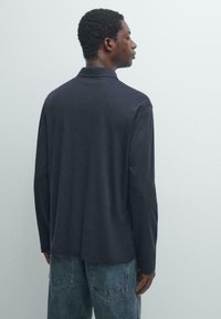 Polo à manches longues bleu marine avec un col classique, une texture lisse et une coupe décontractée, associé à un jean clair avec des poches appliquées.