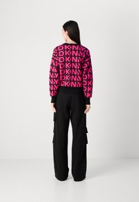 Ryškiai rožinė megzta palaidinė su pasikartojančiu juodu "DKNY" logotipo raštu. Derinama su juodomis laisvomis krovininėmis kelnėmis su šoninėmis kišenėmis.
